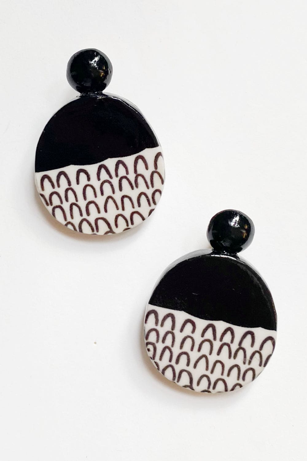 Oval shaped decoupage earrings. The top half is black and the bottom half has upside down u shape patterns.
