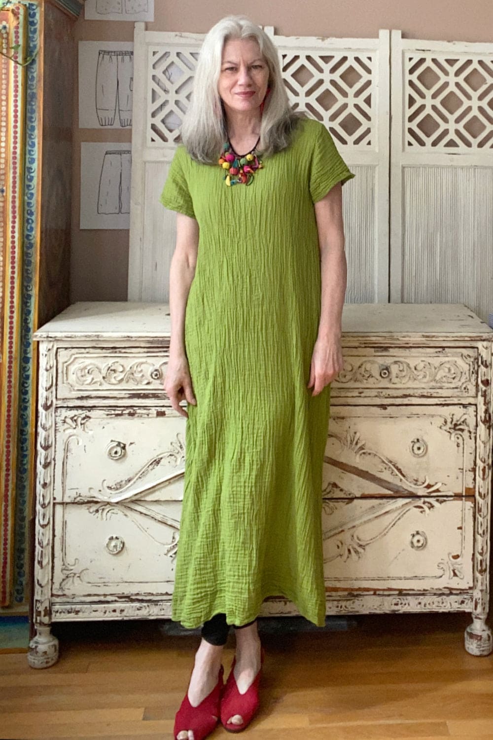 Older woman with long grey hair wearing a moss green short sleeve long cotton dress