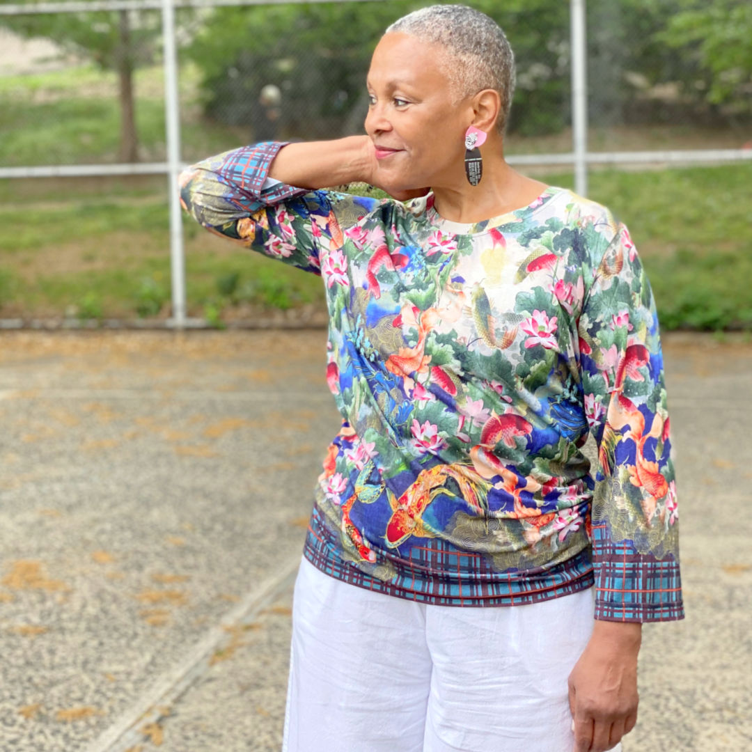 Woman with cropped grey hair wearing a colorful longsleeve tee with cotton pants.
