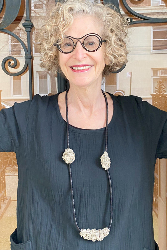 Older happy woman modeling a necklace with wrapped metailci balls against a black cotton top