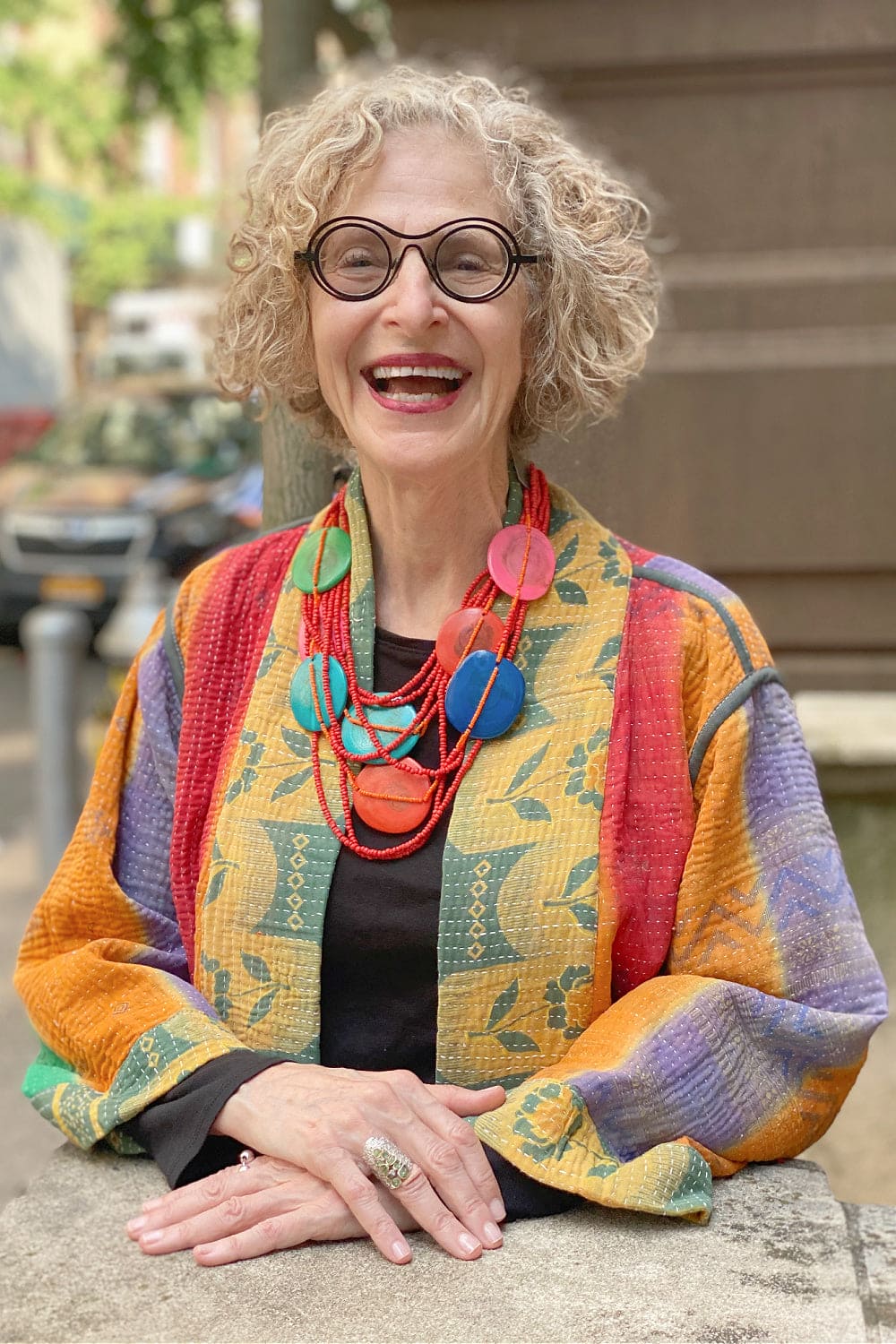 Smiling older woman wearing a bright colorful cotton jacket with colorful necklace.