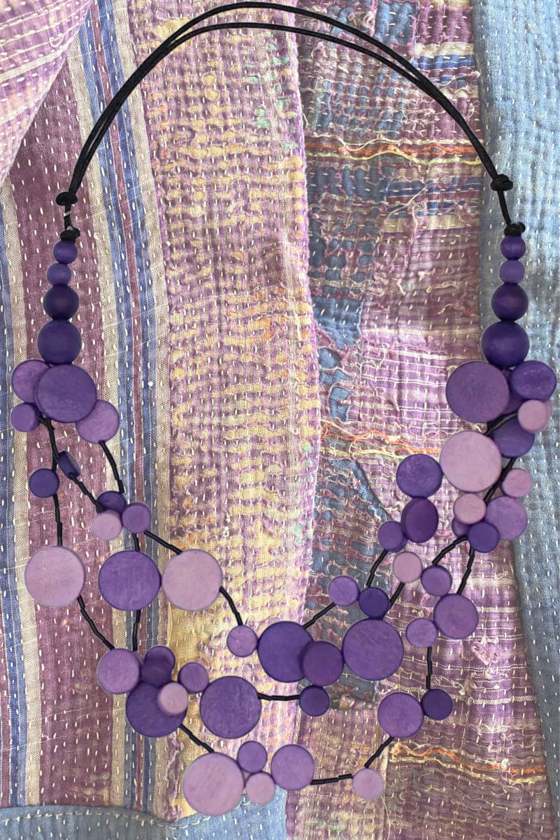 Purple Multi Size Dot Necklace with black adjustable cord resting ontop of purple kantha fabric.