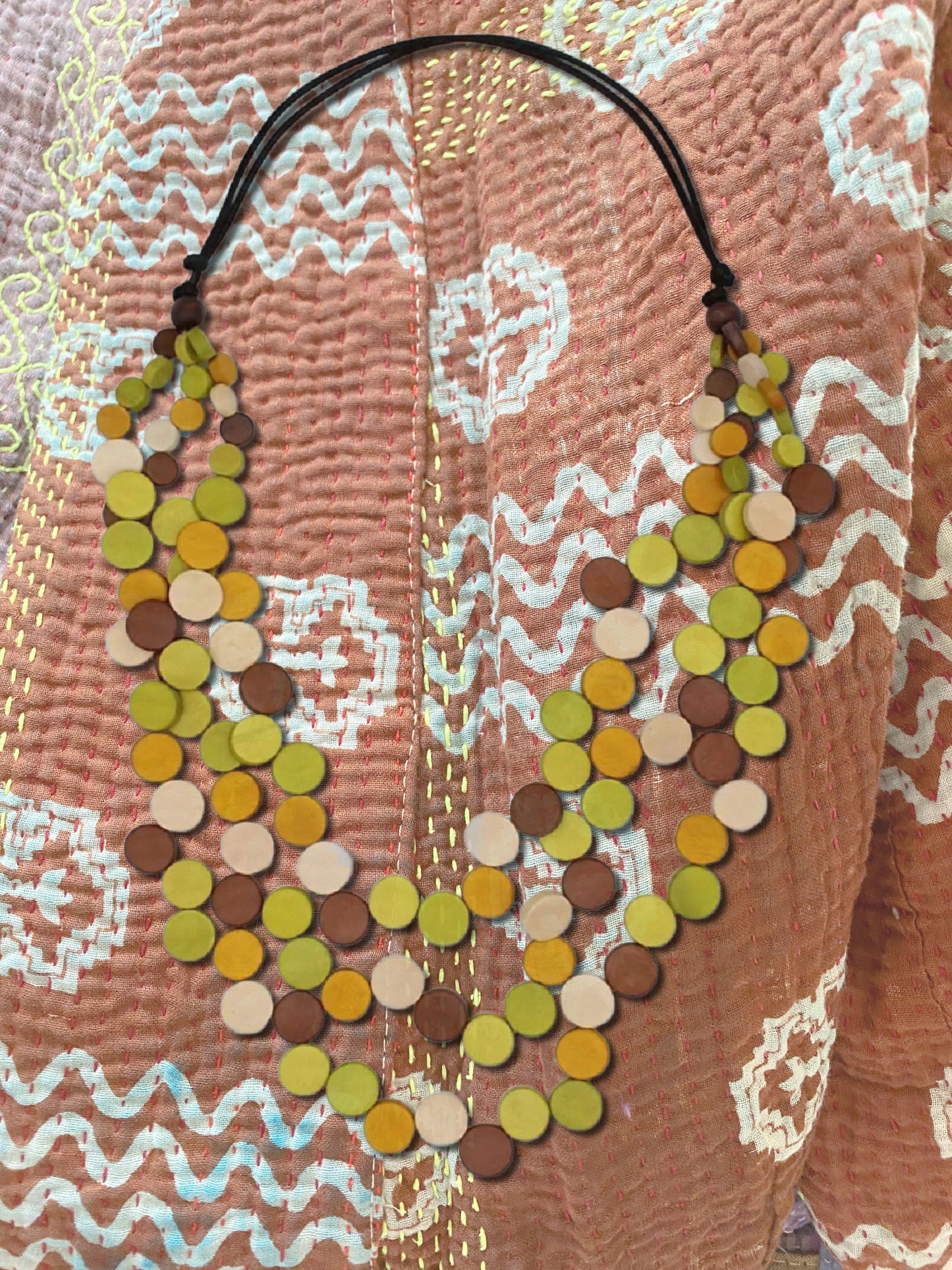 Wooden beaded necklace laying ontop of similar colored kantha jacket.