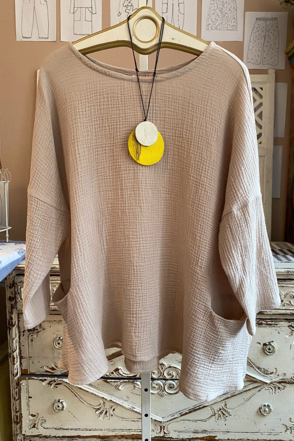 Beige cotton women's top with long sleeves and two front pockets styles with a yellow wooden pendant.