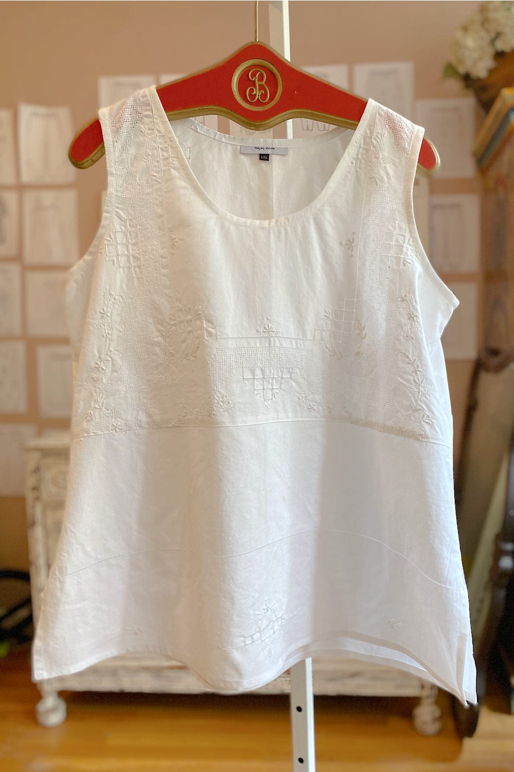 Stitch detailed white cotton tank hanging on a red vintage hanger.