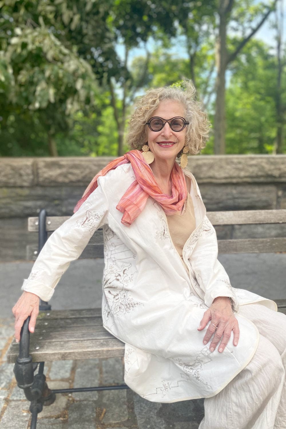 Older woman styled with a silk colorful scarf and curved hem summer jacket.