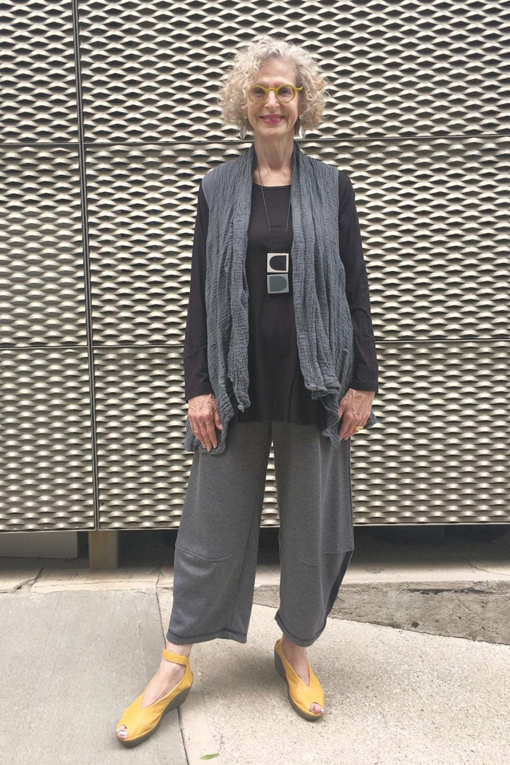 Senior woman with necklength blond hair wearing a stylish casual outfit. Grey vest and loose fit pants with a long sleeve black tee.