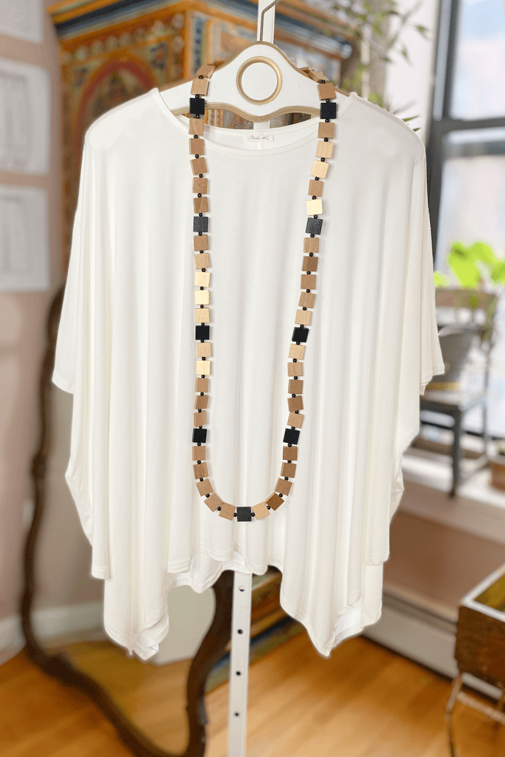Gold and black small wooden squares necklace draped over a loose fit ivory boat neck women's tunic.