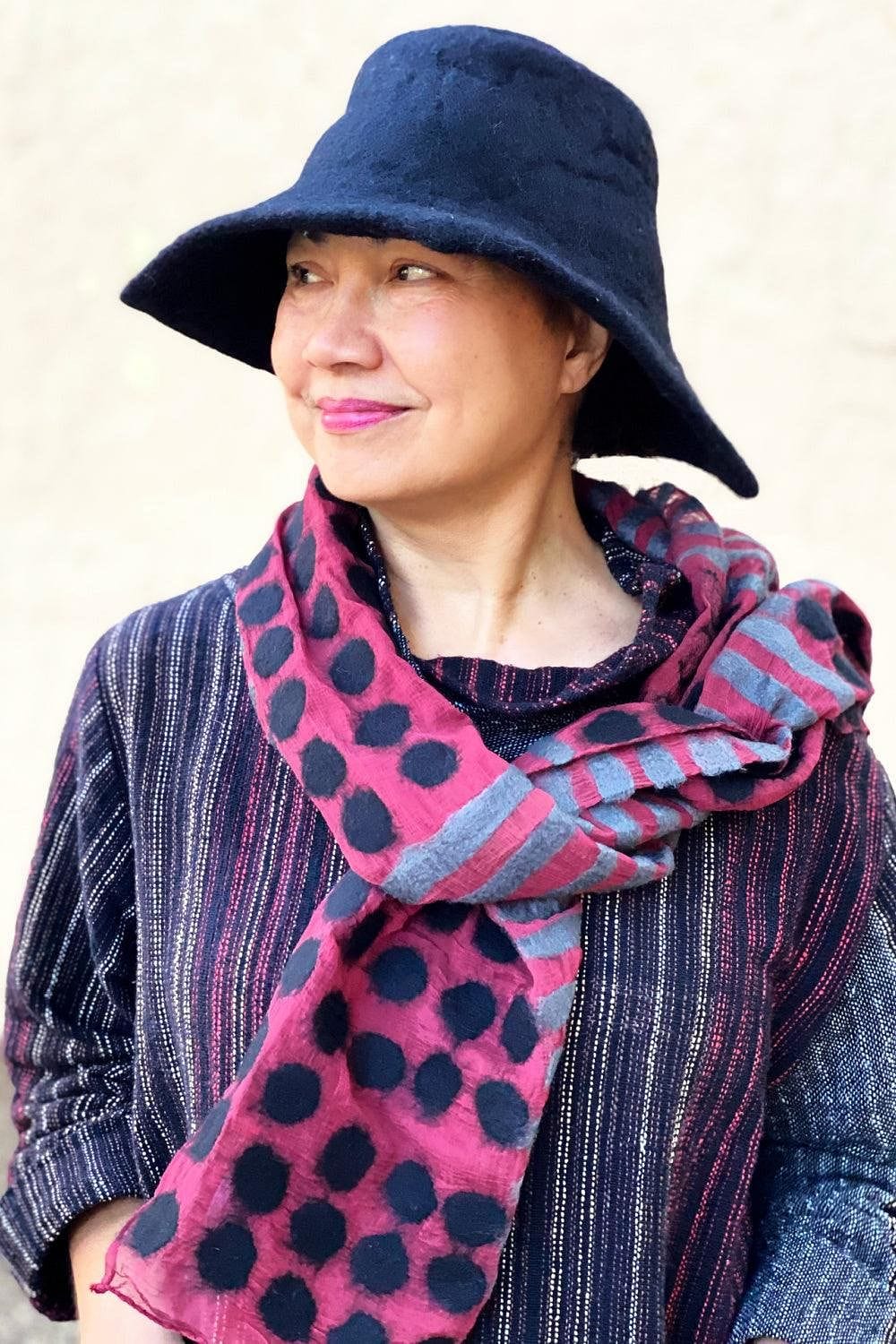 Black Felted bucket hat with wide brim being worn with a plum and grey felted scarf. A smiling woman is also wearing a handwoven pullover. 