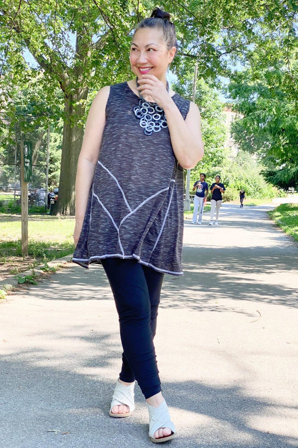 Smiling woman wearing a grey tunic tank with a grey multi loop necklace with black leggings and sandles.