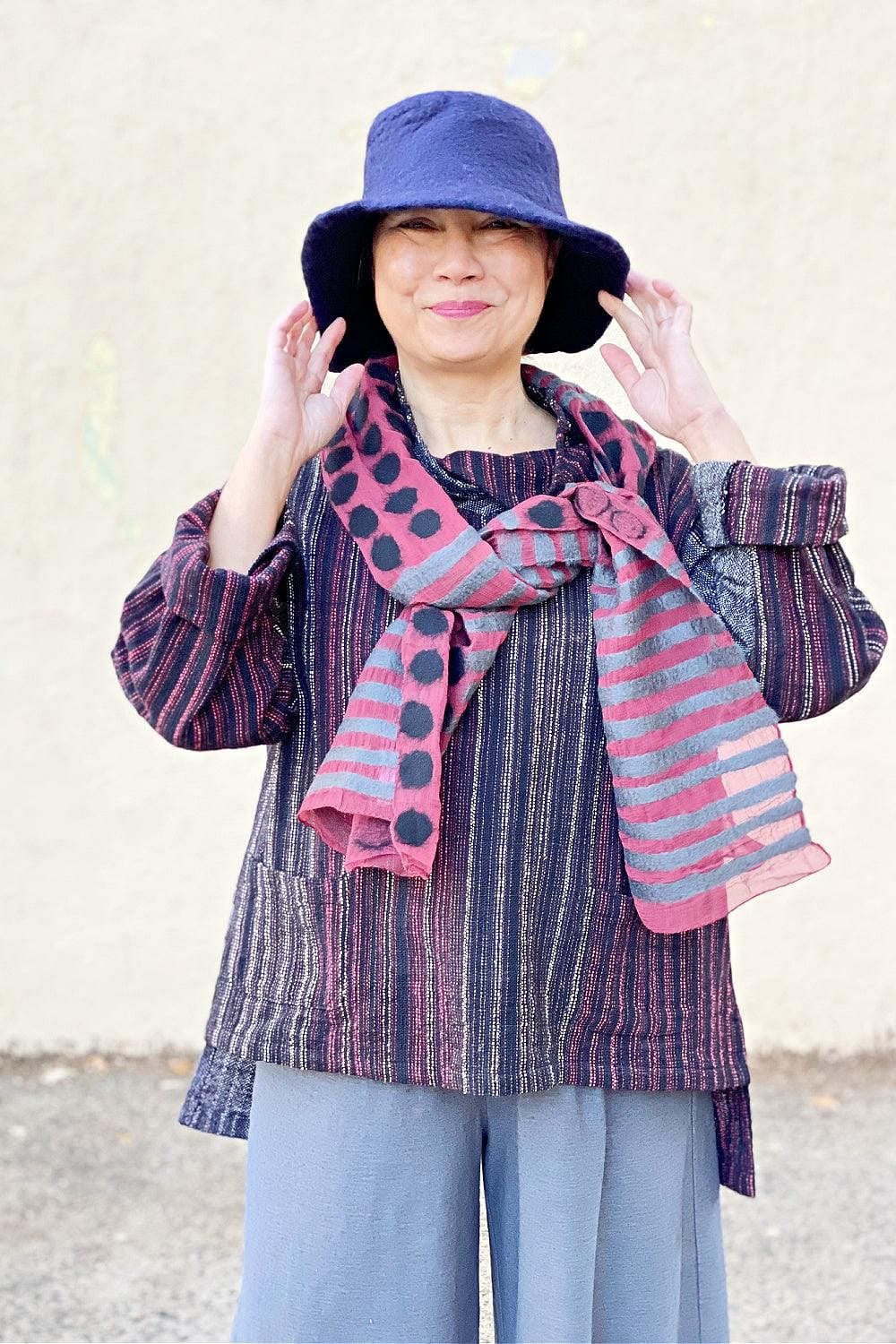 Indigo Blue Felted Hat being worn with a felted scarf. A smiling woman is also wearing a handwoven pullover and grey full cut pants.