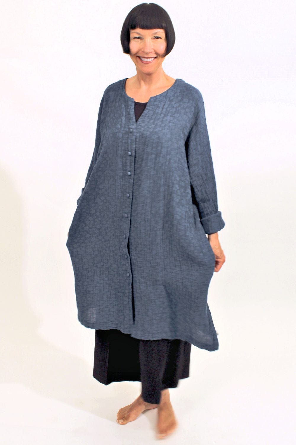 Women's blue long textured linen jacket with fabric covered front buttons and side pockets.