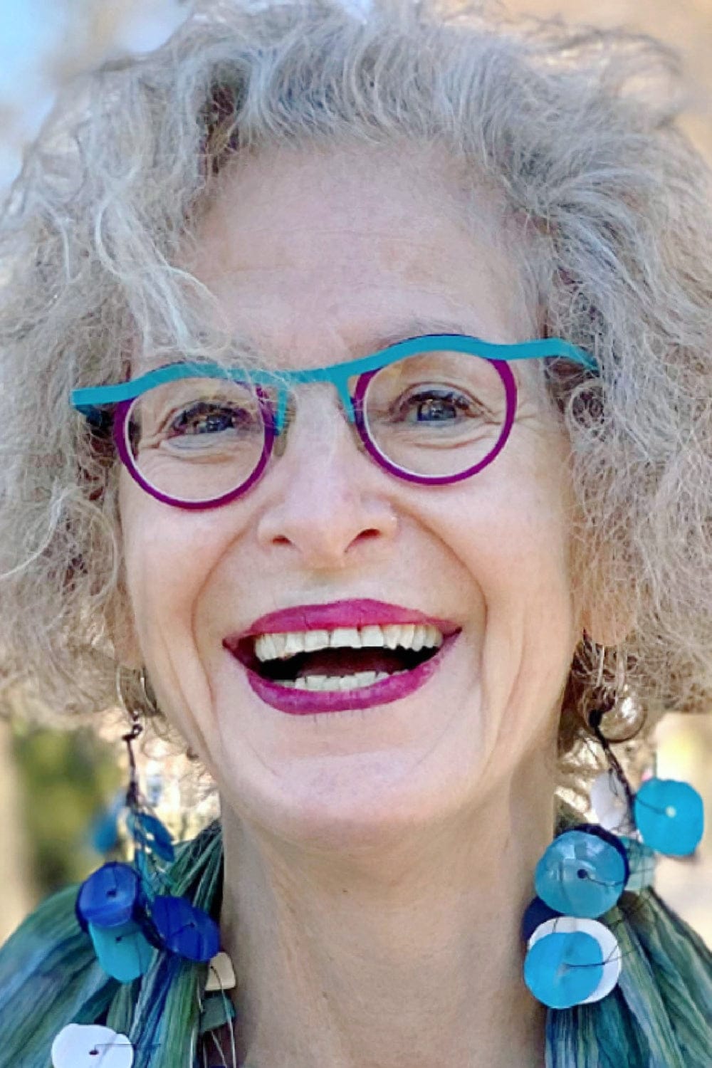 Mulit shades of blue resin earrings worn on a smiling older woman with funky glasses.