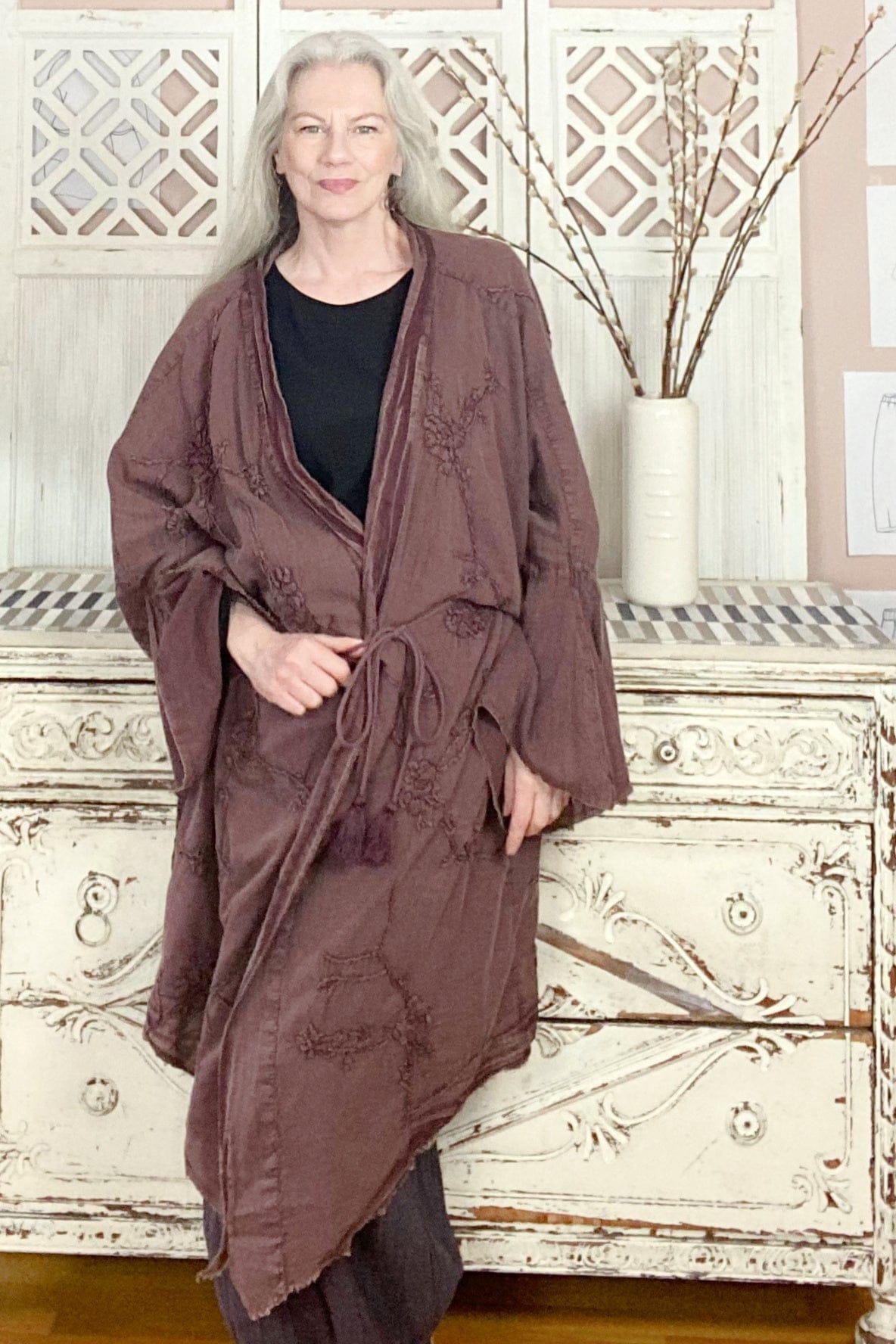 Raisin colored long cotton jacket with embroidery detail worn on a long grey hair woman.