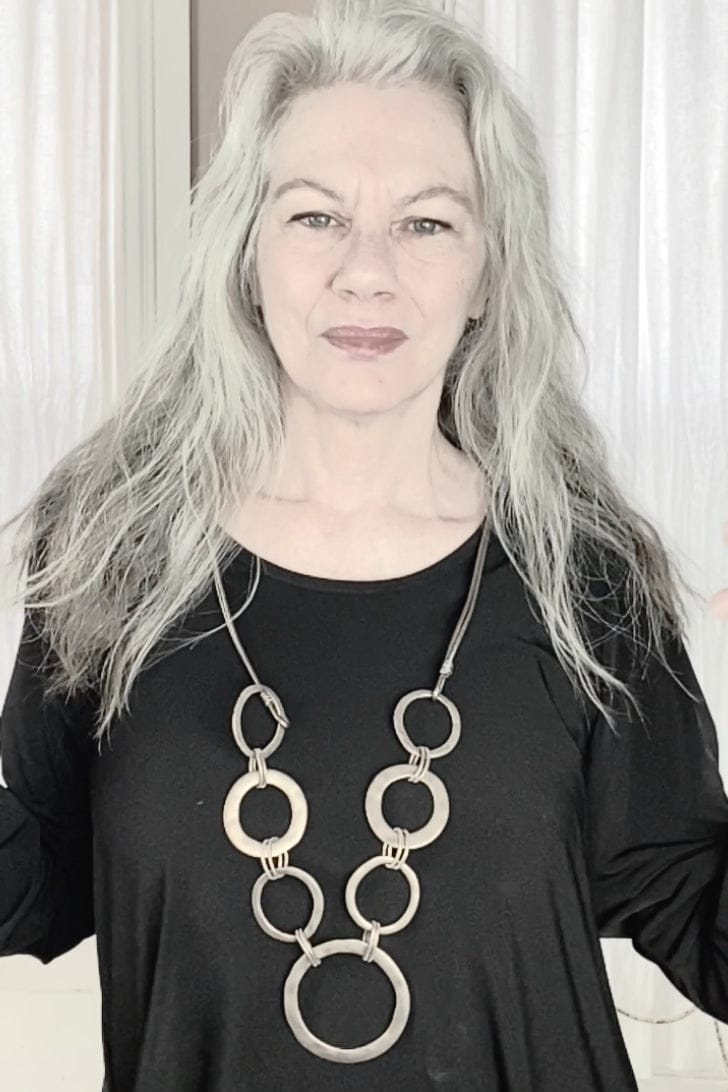 Brass hoop necklace designed with multi sized hoops string on a leather cord. Necklace is modeles on a older grey haired woman.