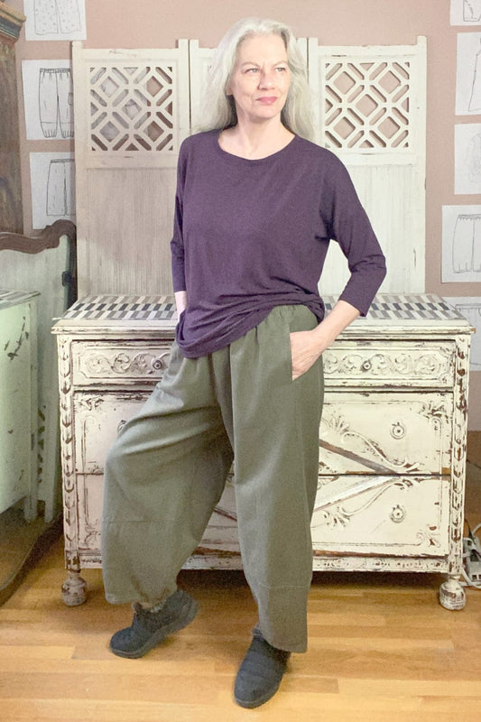 Grey haired woman modeling saddle green colored cotton twill lantern shaped pant with a loose fit purple jersey knit top.