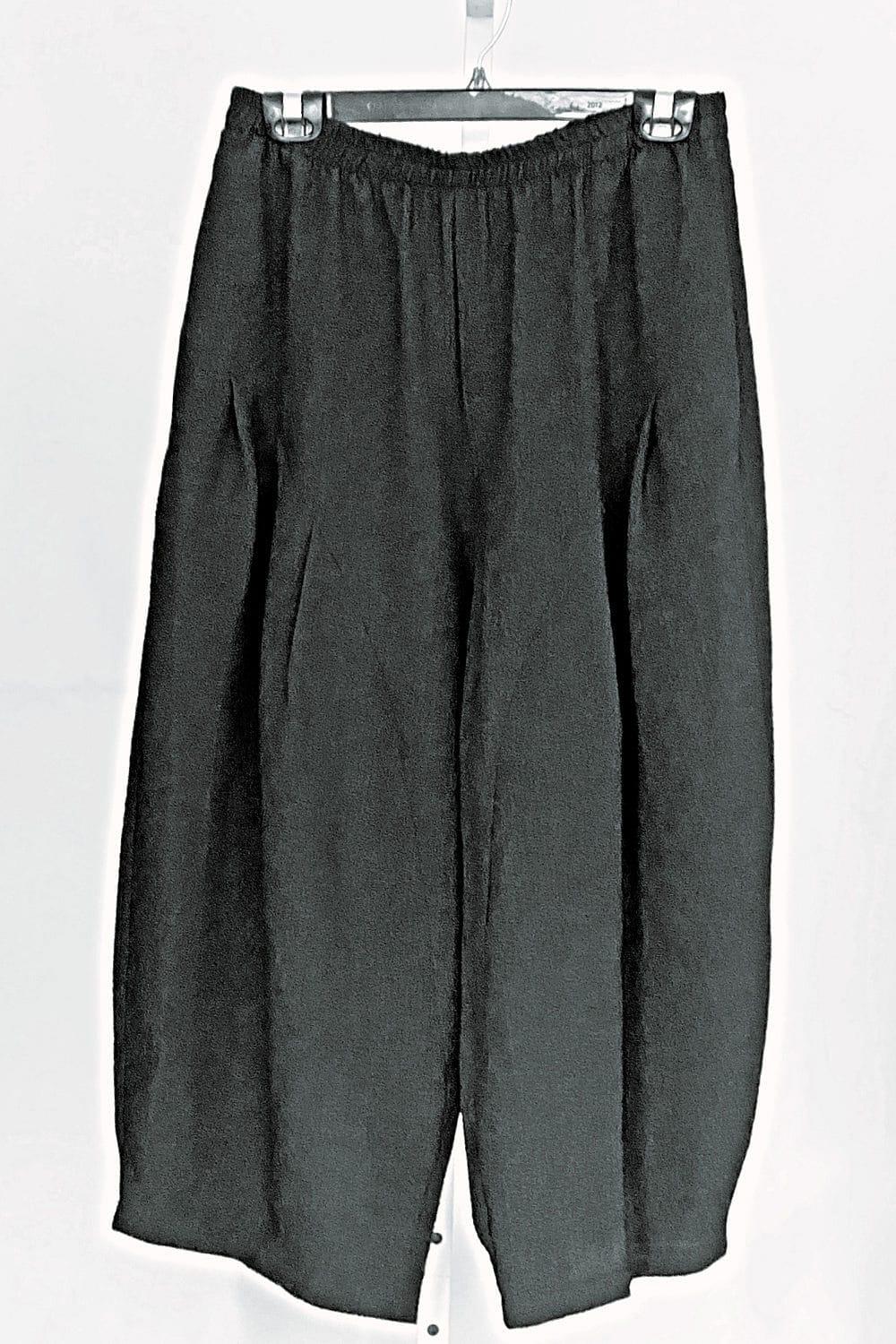 Close up of black full leg pant with front pleast detail and a diagonal hemline. The pant is hanging from a hanger.