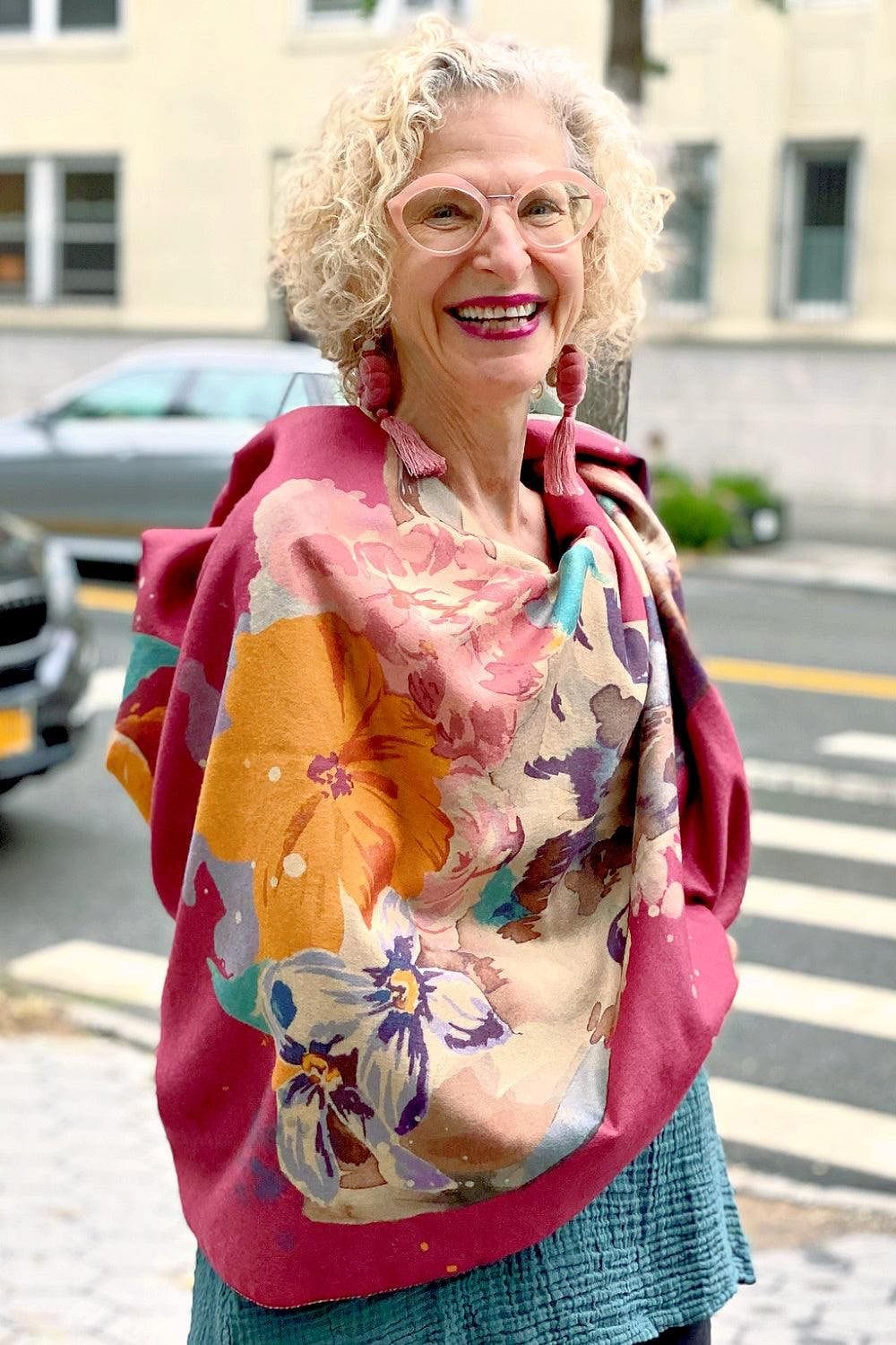 Older woman modeling a women's scarf with a floral woodland print with  soft pinks and yellows with touches of soft blues.