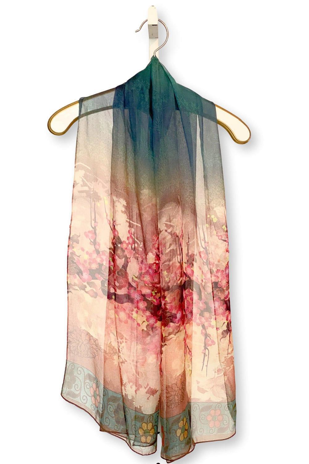 Sheer silk scarf designed with red blossom on tree branches design. It is draped over a creme antique hanger with gold trim. 
