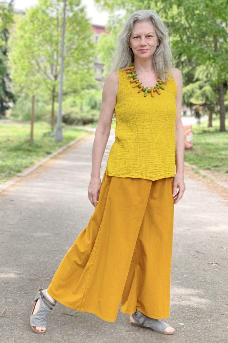 Smiling woman wearing a bright yellow tank with gold Palazzo pants and a matching necklace.