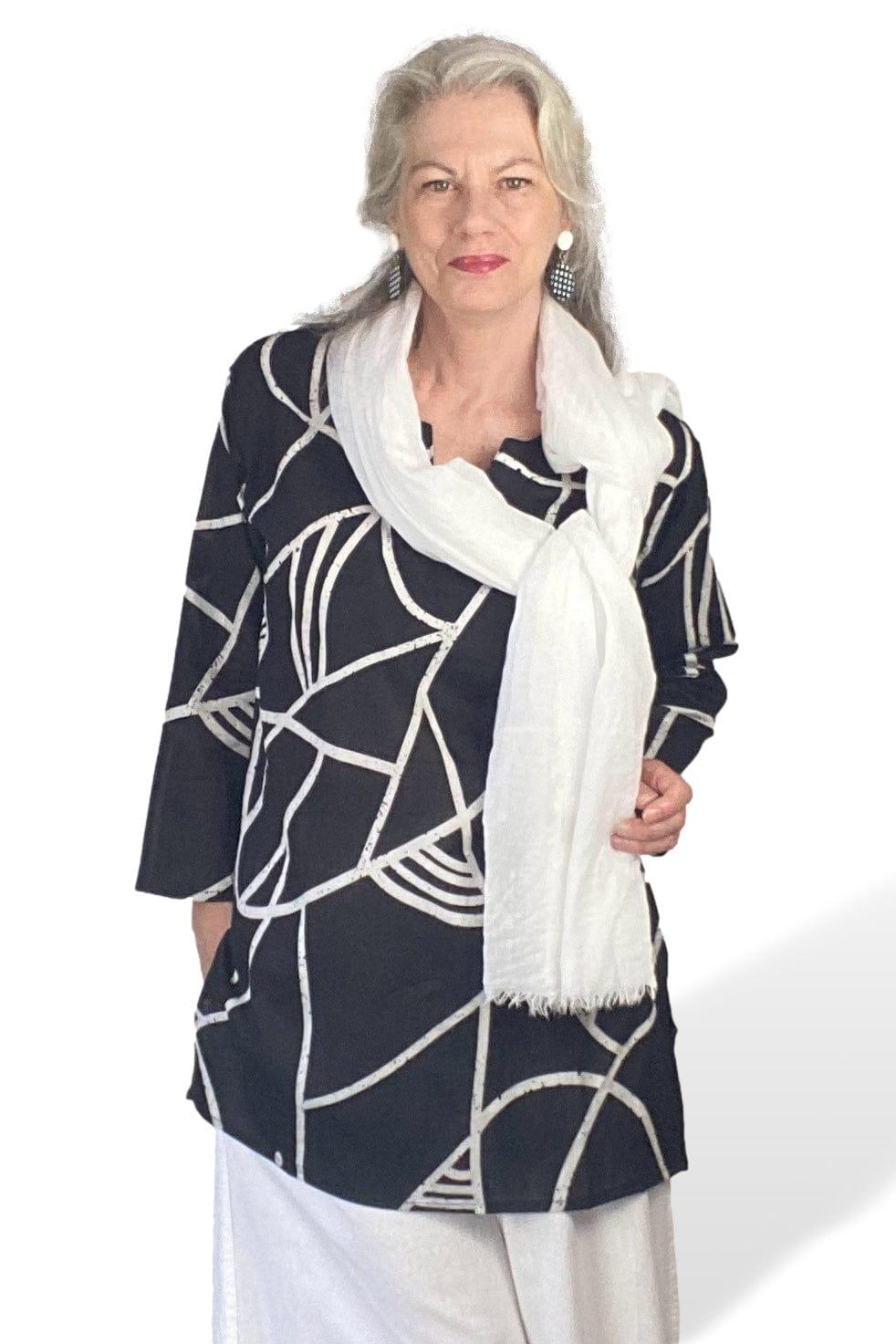 Woman wearing black and white tunic with white pants and scarf with coordination check earrings.