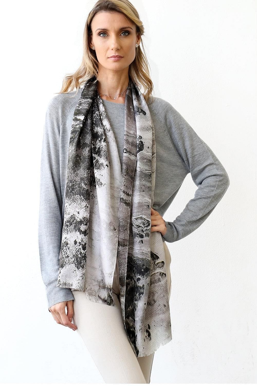 Crushed Pebble Scarf Silk Grey in a long rectangle shape styled over a grey sweater and white pants. Blond haired woman wearing this outfit.