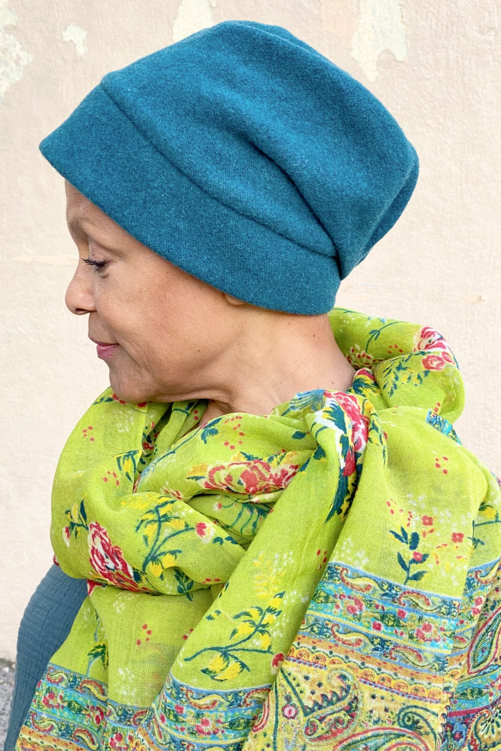 Chartreuse floral and paisly print paper wool scarf resting on the shoulders of an older woman. She is wearing a dark teal winter hat.