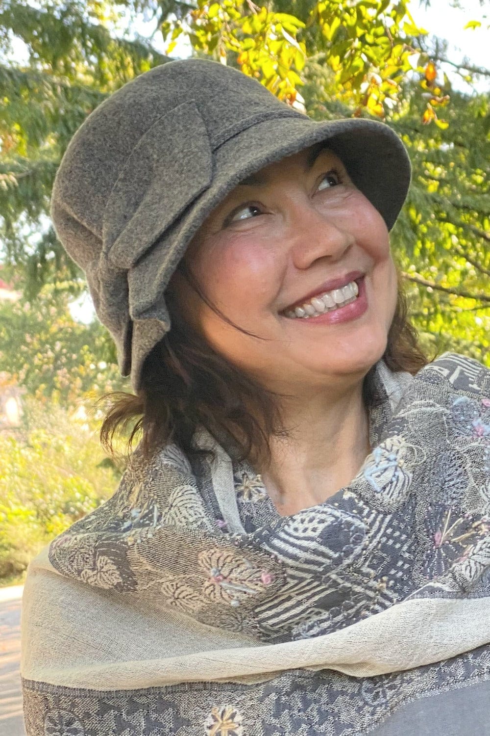 Wool hat with side bow worn on a smiling woman styled with a grey designed scarf.