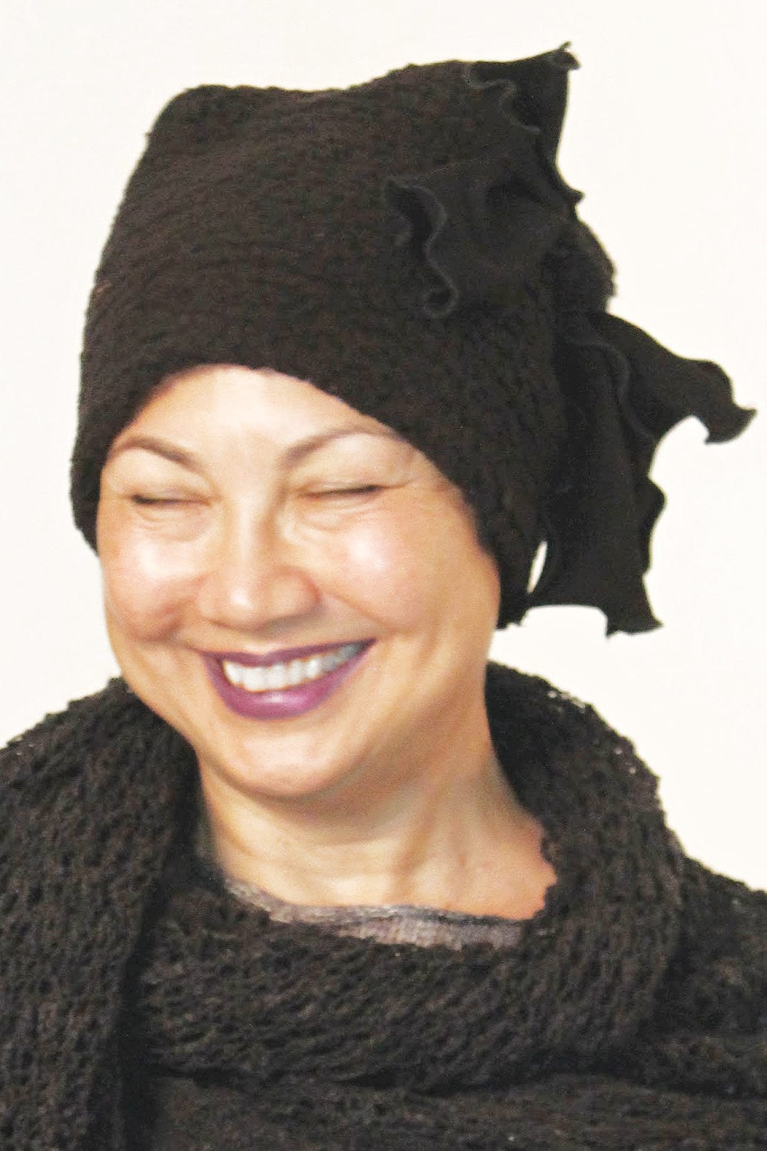 Woman smiling wearing a pull on soft black winter hat with a black side bow.