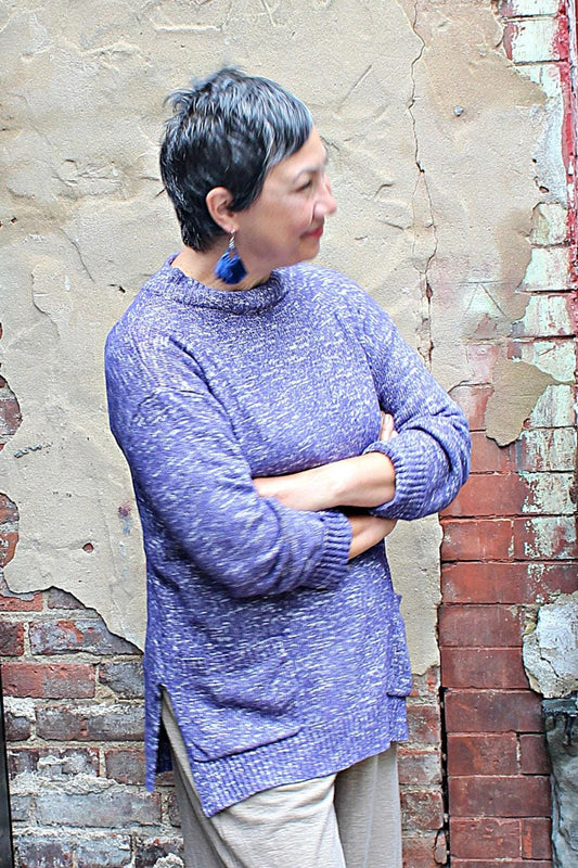 Grey haired woman wearing a high Neck Pullover in a purple color with drop earrings.