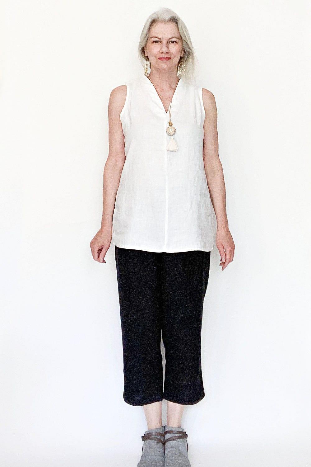 Women with long grey hair pulled back wearing a sleeveless v neck tunic and black taper legged crop pants.