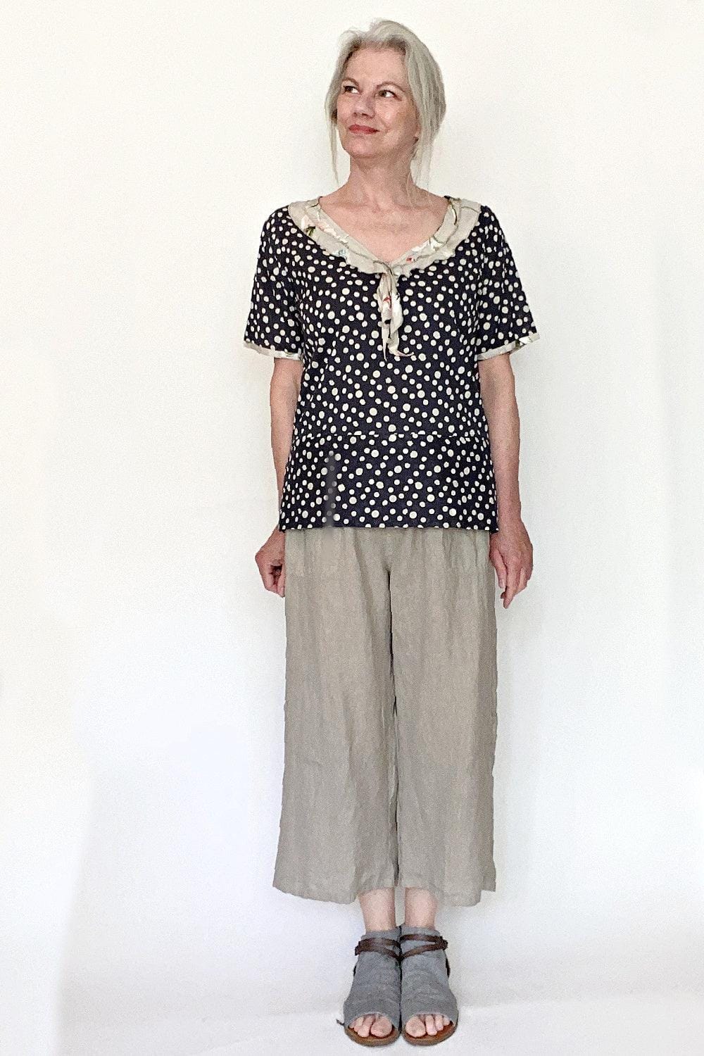 Middle age woman wearing a short sleeve cotton polkla dot v neck blouse with a natural linen loose cut pant and sandels.