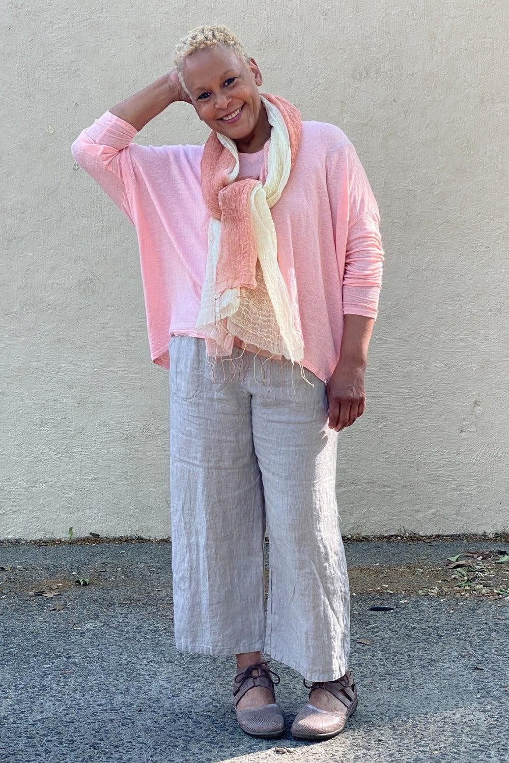 Woman smiling wearing linen loose cut natural color pants with a linen dolman sleeve top and a soft linen scarf.