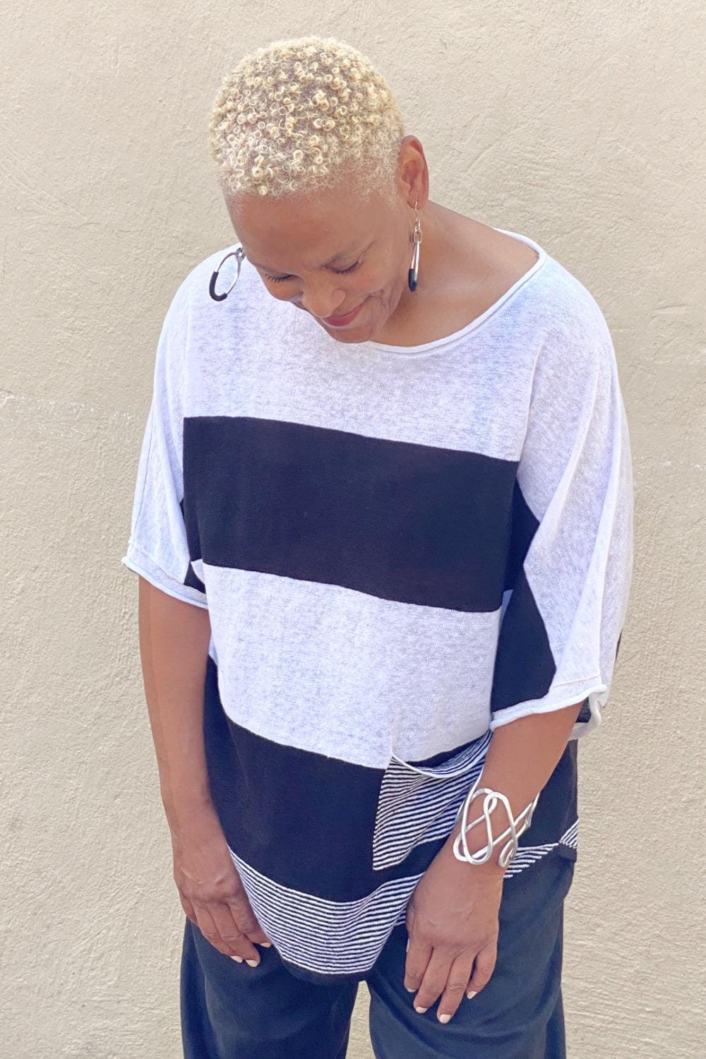 Black and White fine knit linen tee with a small front pocket and a rounded neckline. The sleeve just pass the elbows. The model is wearing a black pair of linen paints and hoop earring and silver bracelet.