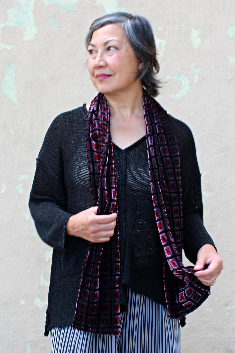 Woman wearing a black loose fit sweater with a black, pink and red cut velvet scarf.