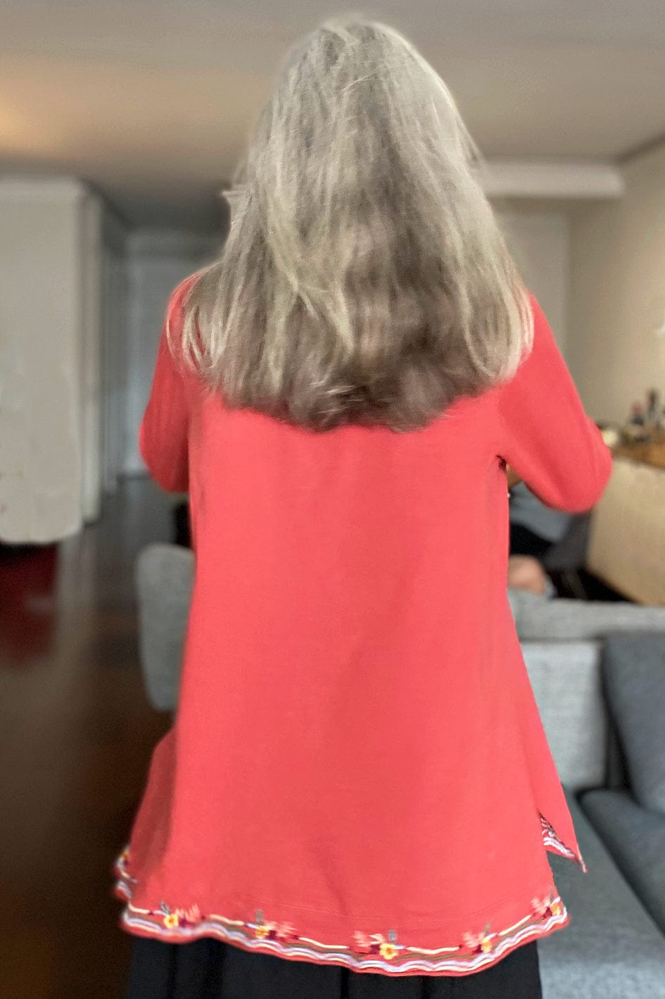 Woman with long grey hair showing back view of aline top with embroidery stitching