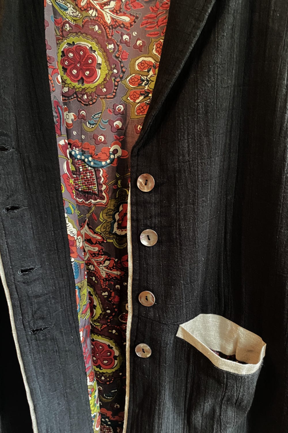 Close up of cotton coat with floral lining. Showing a front pocket trimmed with linen and linen front pipping.