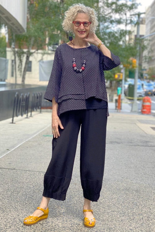 Woman over 60 wearing Black and White Polka Dot women's top with an elastic waisted loose fit black pant and lightwieght wooden statement necklace