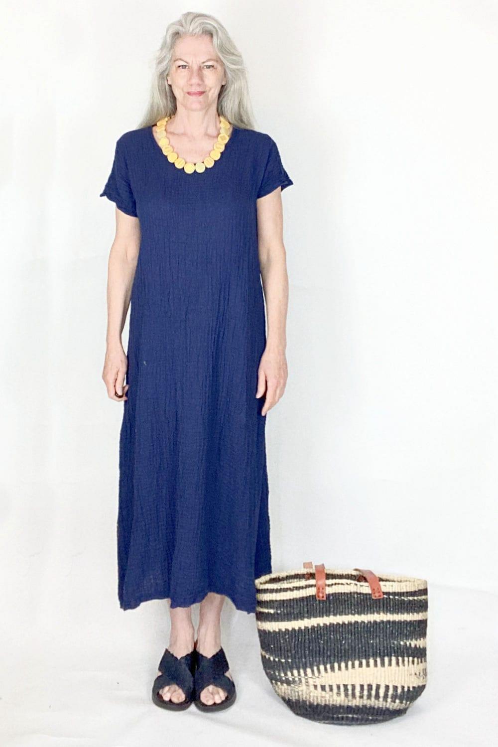 Navy short sleeve long cotton dress being worn by an older smiling woman. She is also wearing a yellow beaded necklace and black sandles