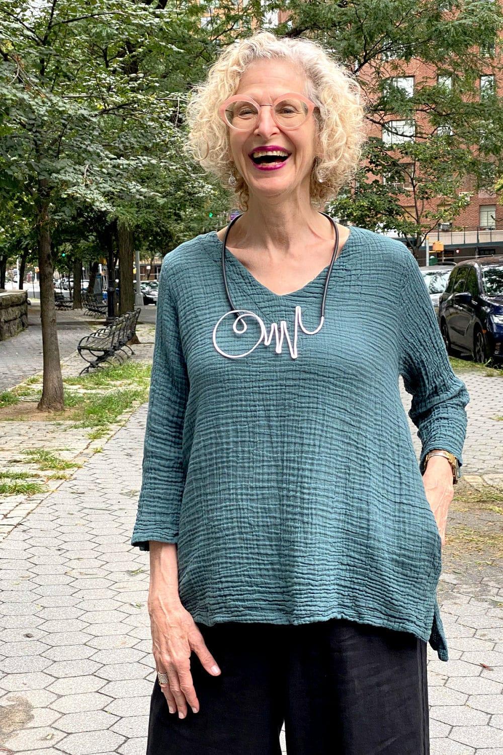 Double Textured Cotton V Neck Top worn on a laughing older model. She is also wearing a silver and black necklace and black loose fit pants.