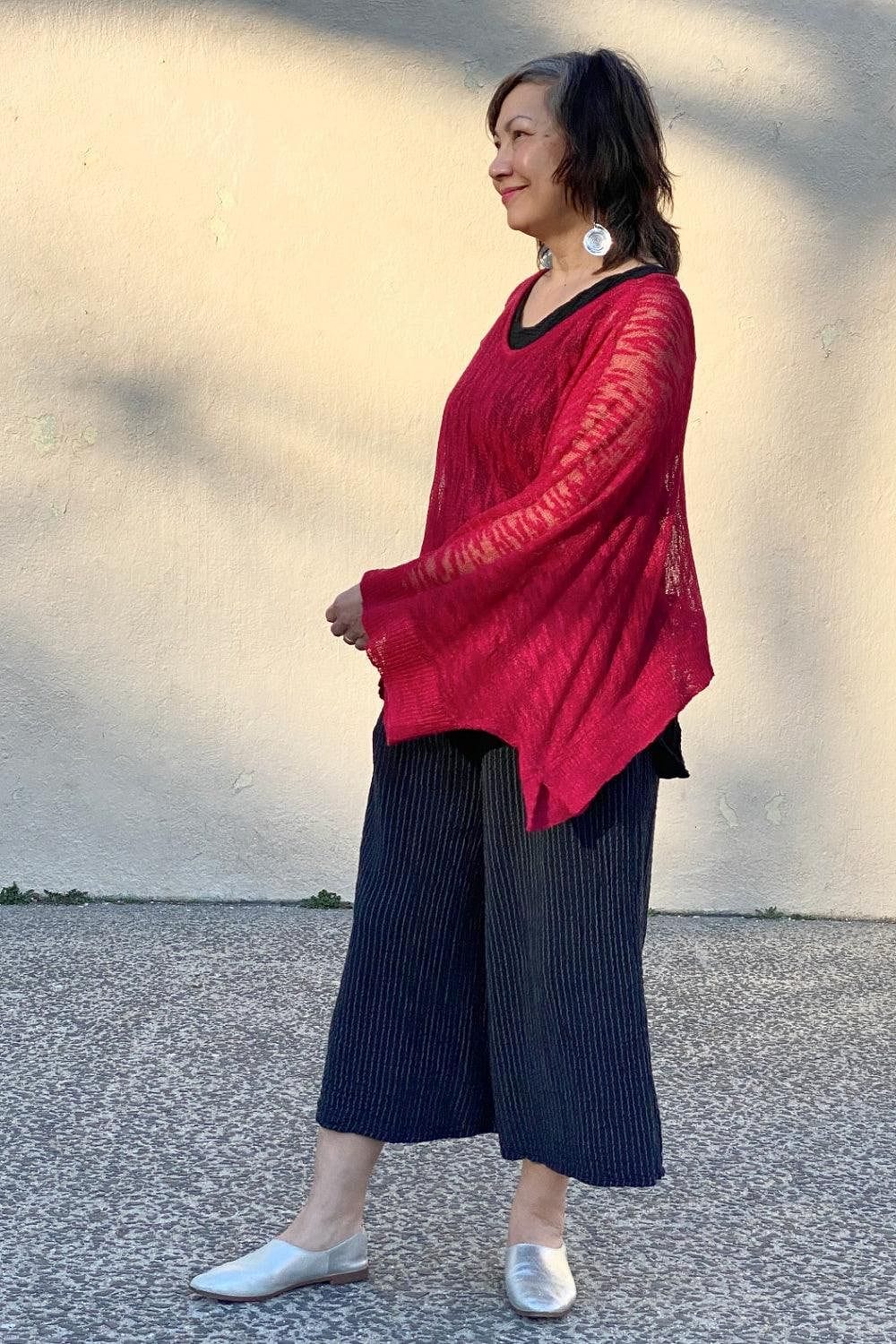 Smiling middle aged woman wearing a red loose fit sweater with wide leg cropped pants and fun earrings.