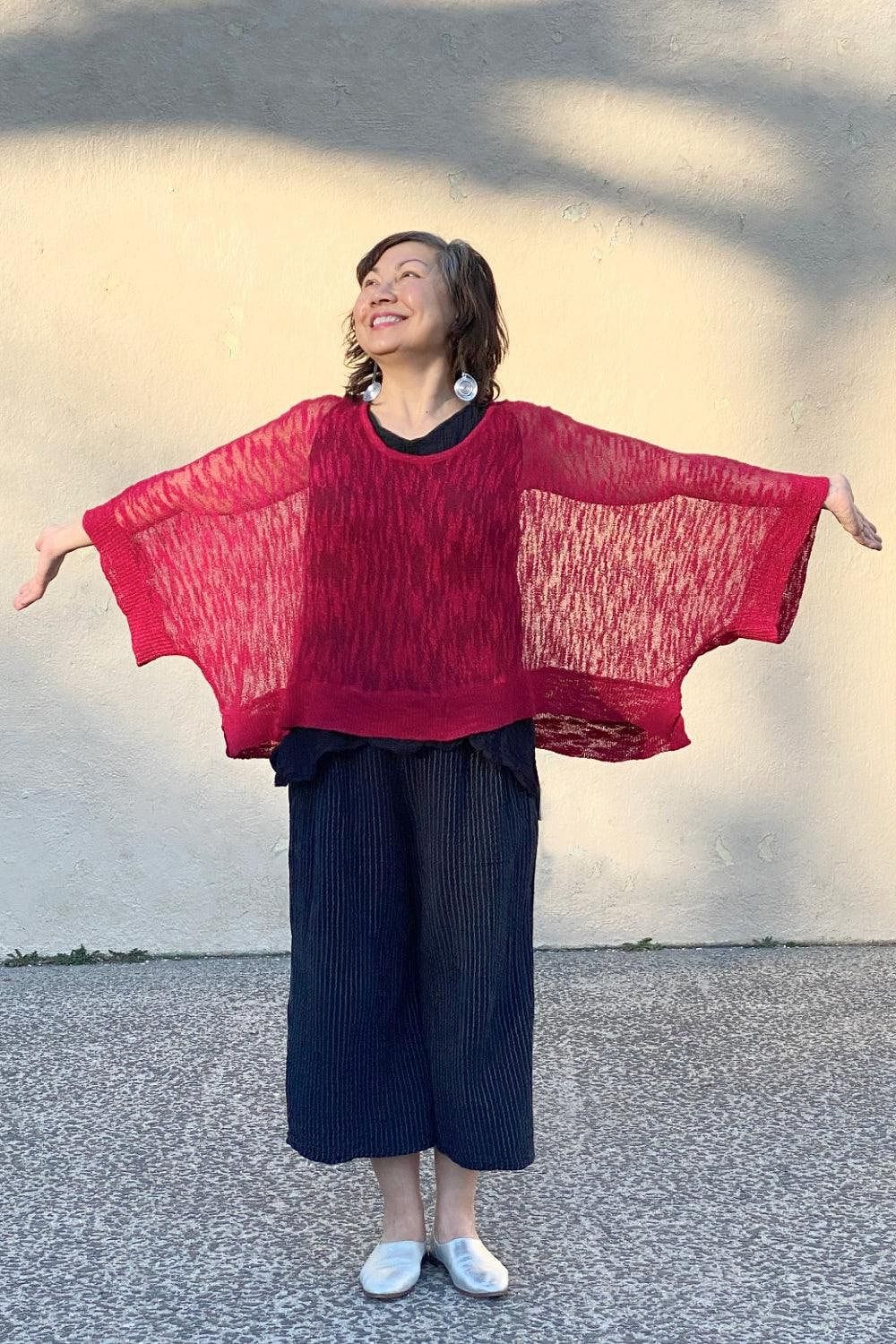 Smiling middle aged woman wearing a red loose fit sweater with wide leg cropped pants and funky earrings.