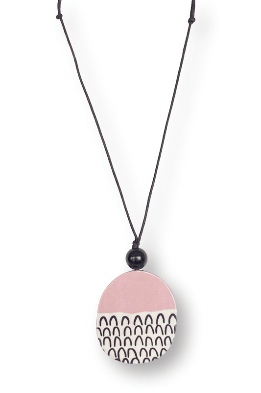 Light wooden pendant hanging from a waxed black adjustable cord. Pink color with a black and white upside down fleck design wih one black bead sitting on top of oval pendant