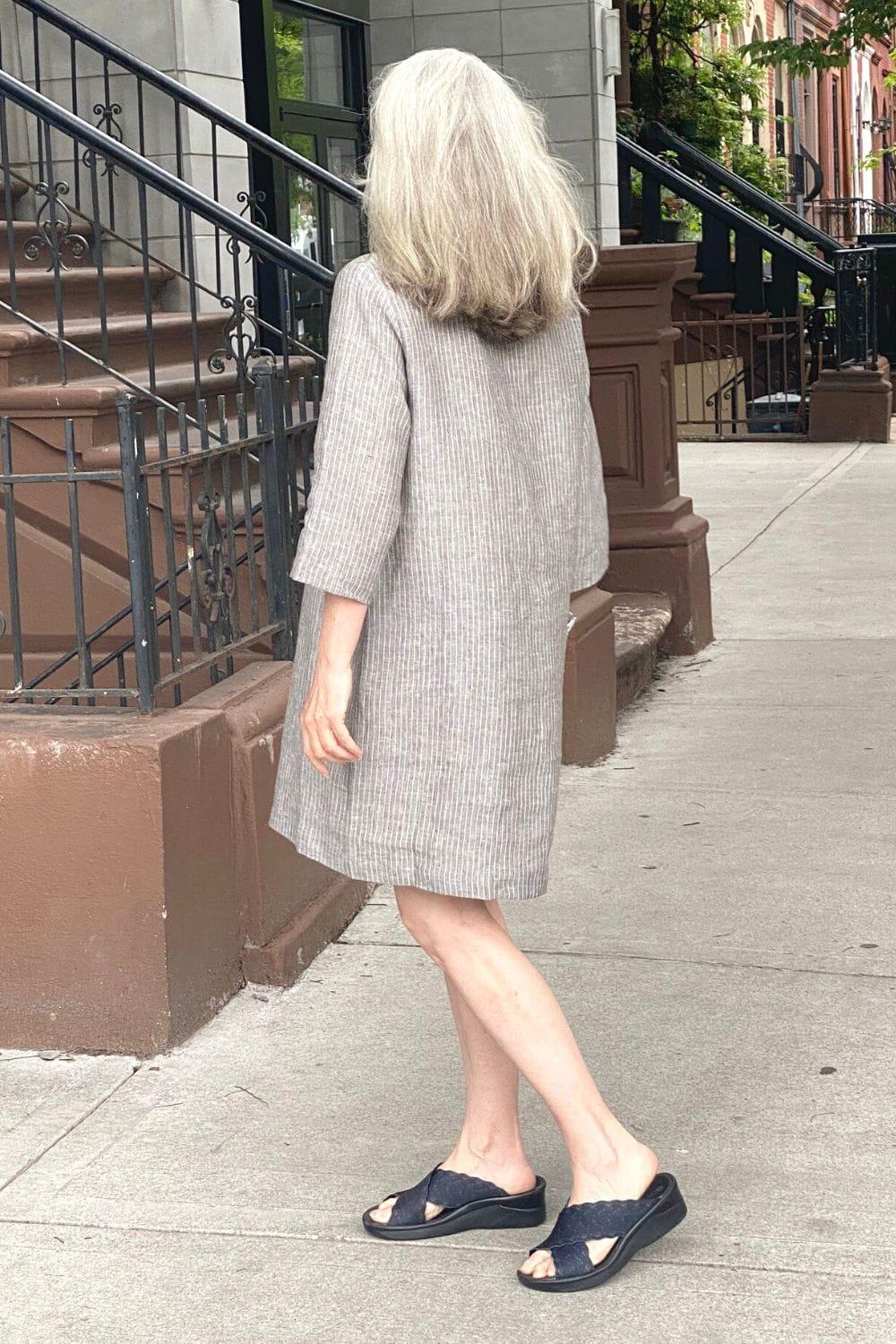 Back view of a woman with long grey hair wearing a grey pinstripe linen knee length dress