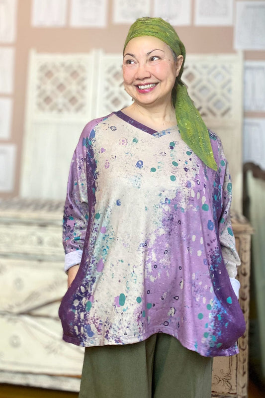 Smiling woman wearing a v neck 2 pocket aline sweater with a green head scarf and loose fit pants.
