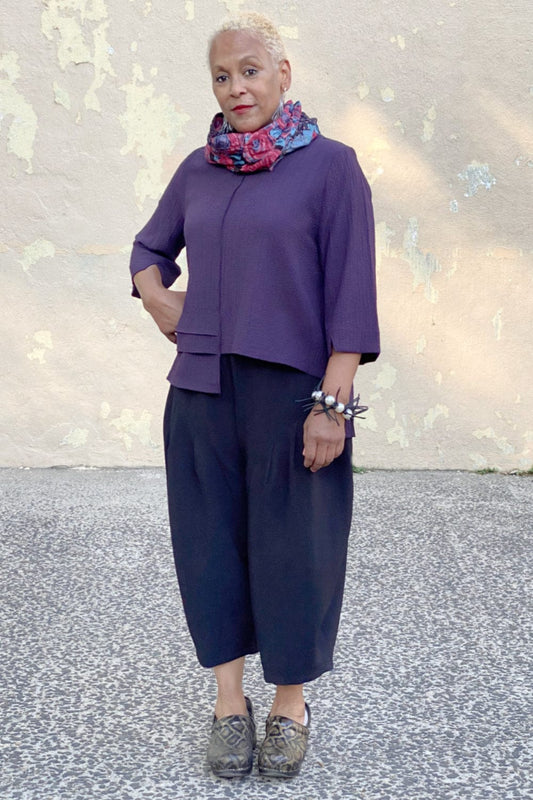 Older woman modeling a boxy plum colored top with loose fit crop pants. Styles with a funky bracelet and colorful scarf.