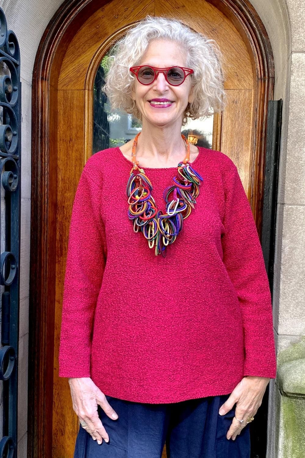 Smiling older woman wearing a pretty Raspberry Cotton Sweater with a multi color loop necklace.