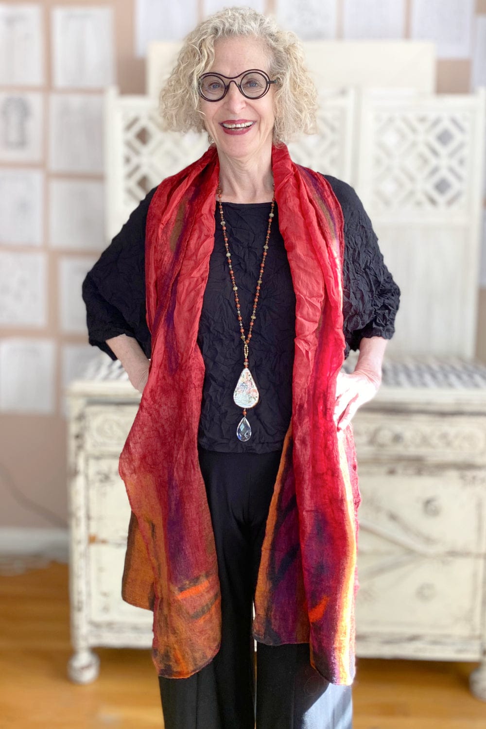 Red felt and silk scarf worn over a black top and pants accessorized with a pendant necklace.