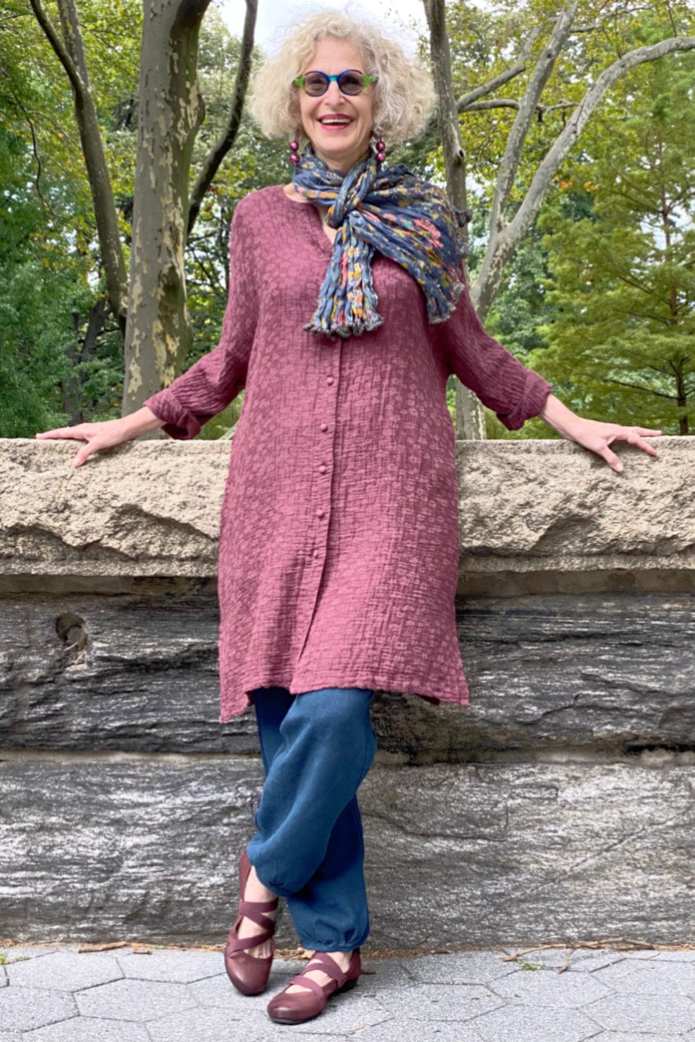 Womens rose colored long textured linen jacket with fabric covered front buttons and side pockets. Cotton blue floral scarf is styled with blue linen pants.