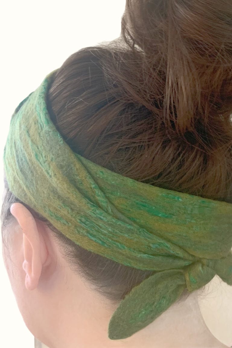 Close up of a green sari head scarf tied around a women's head and knotted in the baclk of her neck.
